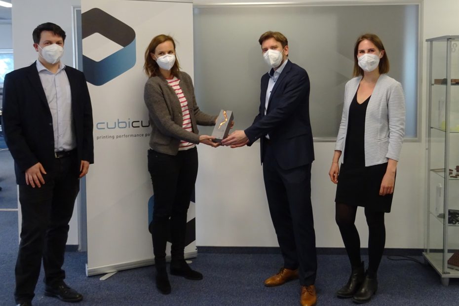 Eine Vertreterin der WKO überreicht dem Geschäftsführer von Cubicure den Exportpreis 2020 in Bronze. Eine Mitarbeiterin und ein Mitarbeiterin stehen neben ihnen. Alle tragen FFP2-Masken.