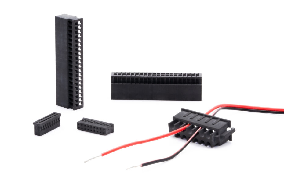 Different black 3D printed connectors on a white background. The foremost component has snap-fits. There is a black and red cable threaded through its holes.